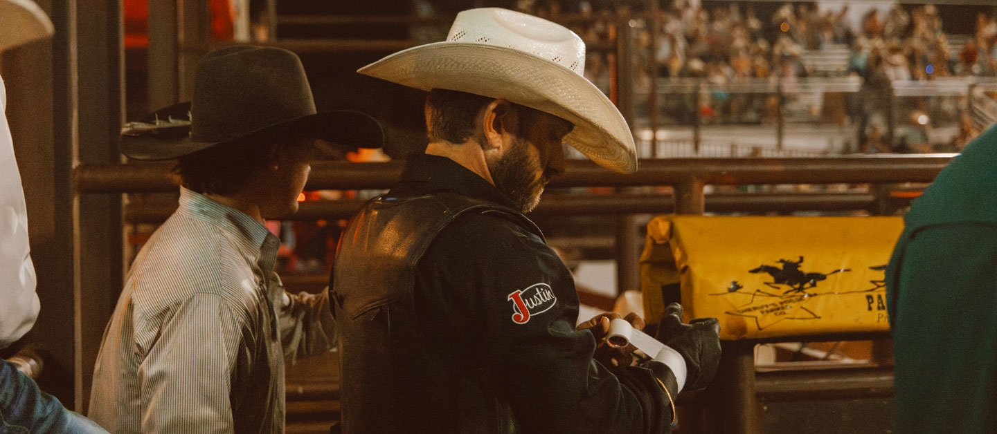 Un hombre con camisa negra y sombrero de vaquero, de pie y prepar&aacute;ndose en un rodeo.